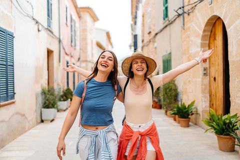 Urlaub versichern: Zwei Freundinnen laufen im Urlaub lachend durch eine spanische Innenstadt