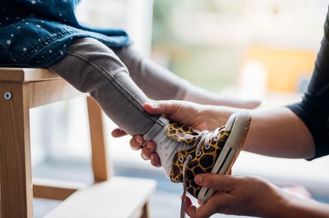 Einem Kind wird ein Schuh angezogen – zur Erziehung gehört es, dass Kinder das erlernen