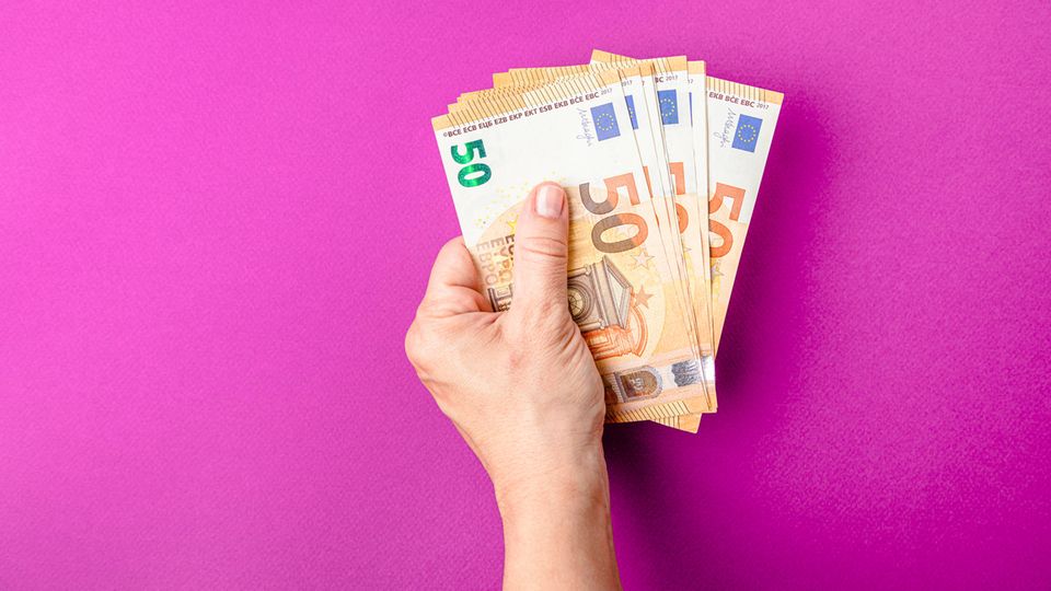 Eine Hand hält mehrere 50-Euro-Scheine vor einem rosa Hintergrund