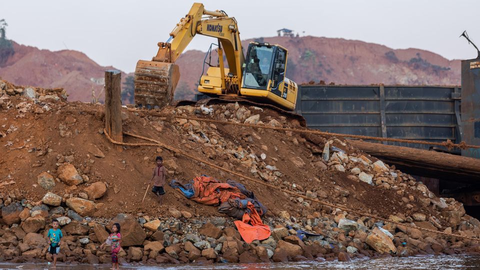 Kinder spielen im verschmutzten Wasser, während über ihnen ein Bagger nickelhaltiges Gestein abräumt