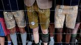 Hinter dem Gitter sieht man wartende Leute in Lederhosen