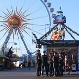 Polizisten stehen an einem Stand, dahinter kann man ein Riesenrad sehen