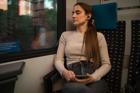 Eine Frau schläft mit Sleepbuds im Zug