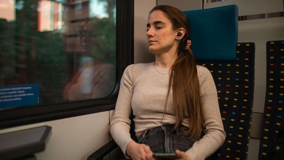 Eine Frau schläft mit Sleepbuds im Zug