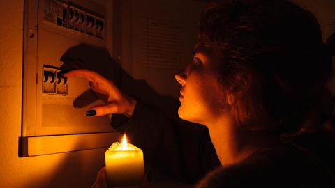 Balkonkraftwerk bei Stromausfall nutzen: Frau steht mit Kerze in der Hand vor einem Sicherungskasten.