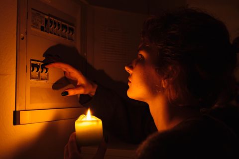 Balkonkraftwerk bei Stromausfall nutzen: Frau steht mit Kerze in der Hand vor einem Sicherungskasten.
