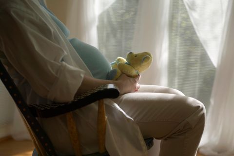 Eine Frau hält einen Teddybär vor ihrem Schwangerschaftsbauch