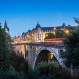 Die Adolphe-Brücke in Luxemburg, während der Abenddämmerung. Man sieht flackernde Lichter und Verkehr auf den Straßen