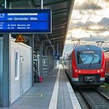 Roter RE-Zug hält auf einem Bahnhof in Deutschland. Eine Anzeige kündigt die Weiterfahrt nach Gemünden an.