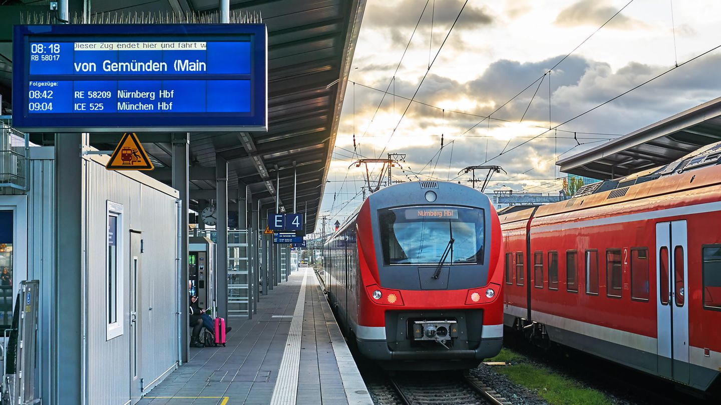 Deutschland: Das Deutschlandticket Roter RE-Zug hält auf einem Bahnhof in Deutschland. Eine Anzeige kündigt die Weiterfahrt nach Gemünden an.