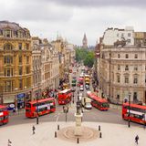 Vogelblick auf eine Straße, die auf den Big Ben zuläuft. Es ist viel Verkehr, im Vordergrund sind viele rote Busse.