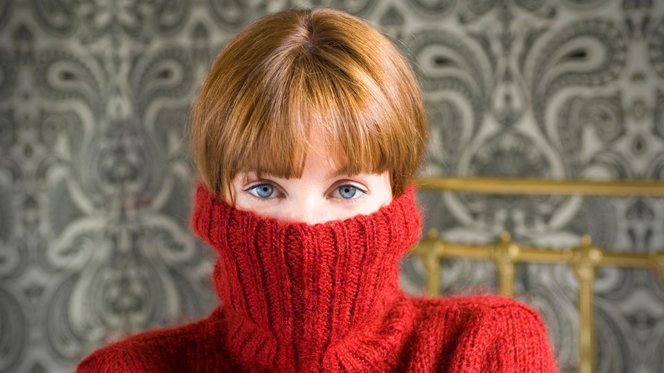 Unsicherheit: Junge Frau hat einen Wollpulli bis zur Nase hochgezogen