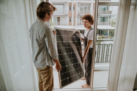Erstes Balkonkraftwerk: Zwei junge Menschen tragen ein Solarmodul auf den Balkon.