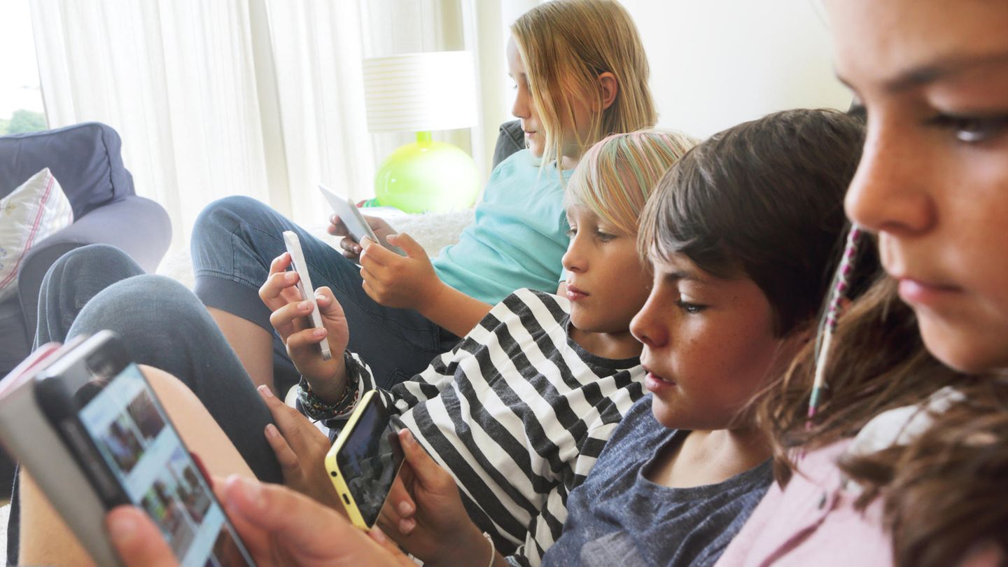 Vier Kinder sitzen nebeneinander, jedes guckt auf sein Telefon