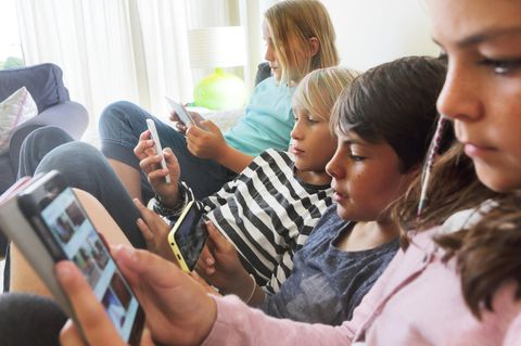 Vier Kinder sitzen nebeneinander, jedes guckt auf sein Telefon