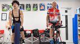 Ein junger und ein alter Mann trainieren nebeneinander auf dem Rad im Fitnessstudio