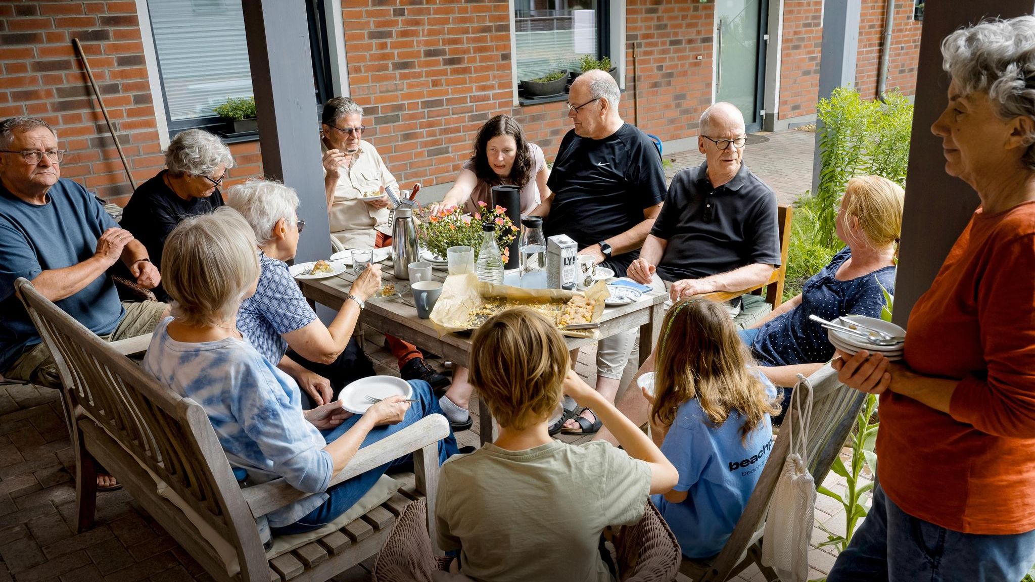 Menschen verschiedenen Alters sitzen beim Co-Housing zusammen am Tisch und essen Kuchen
