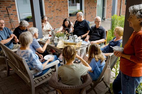 Menschen verschiedenen Alters sitzen beim Co-Housing zusammen am Tisch und essen Kuchen