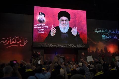 Anhänger in Beirut erheben ihre Fäuste und jubeln, während sie eine Rede Nasrallahs im Dunkeln vor einem riesigen Schirm hören