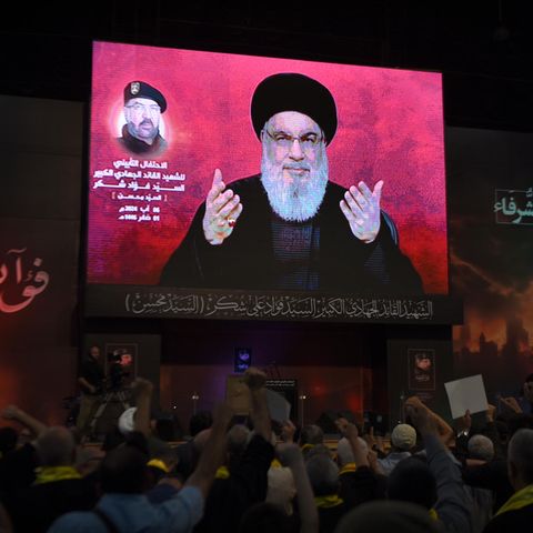 Anhänger in Beirut erheben ihre Fäuste und jubeln, während sie eine Rede Nasrallahs im Dunkeln vor einem riesigen Schirm hören