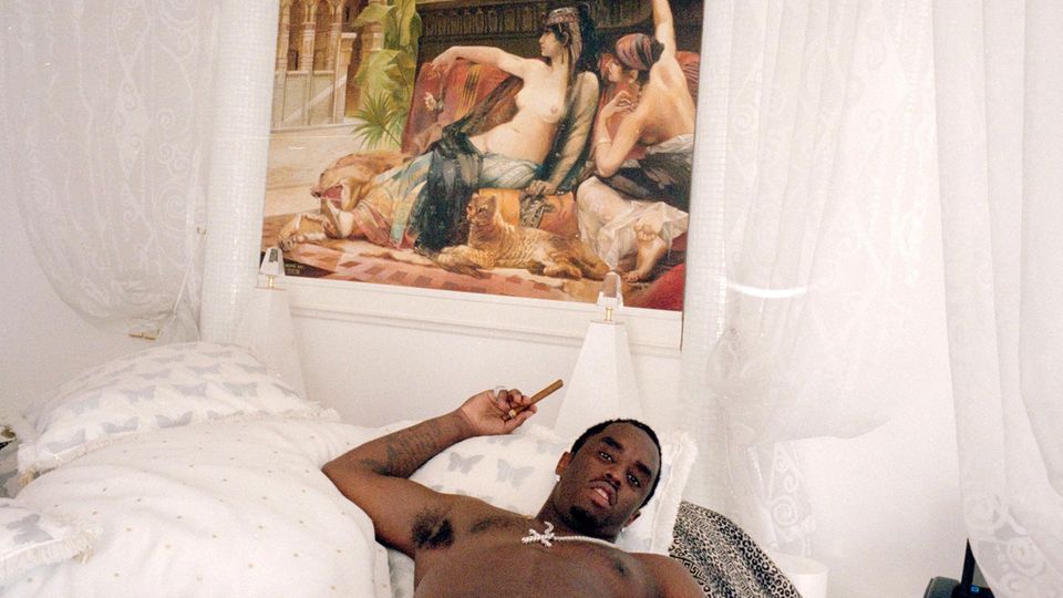 P. Diddy in einem Bett mit einer Zigarre in der Hand und einem Gemälde über dem Bett