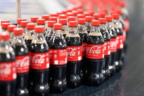 Mit Coca Cola gefüllte PET-Flaschen fahren auf dem schwarzen Fließband vorbei