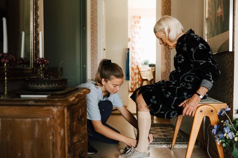 Eine Pflegerin hilft einer älteren dame beim Schuhe anziehen