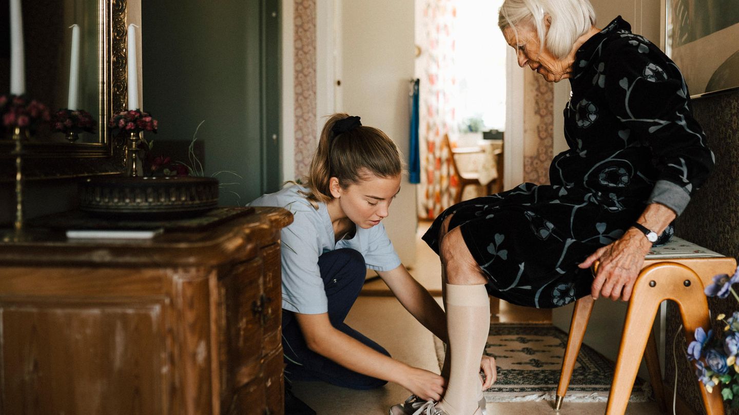 Eine Pflegerin hilft einer älteren dame beim Schuhe anziehen