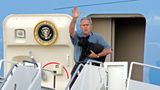 George W- Bush hält auf der Treppe eines Flugzeugs einen schwarzen Hund im Arm
