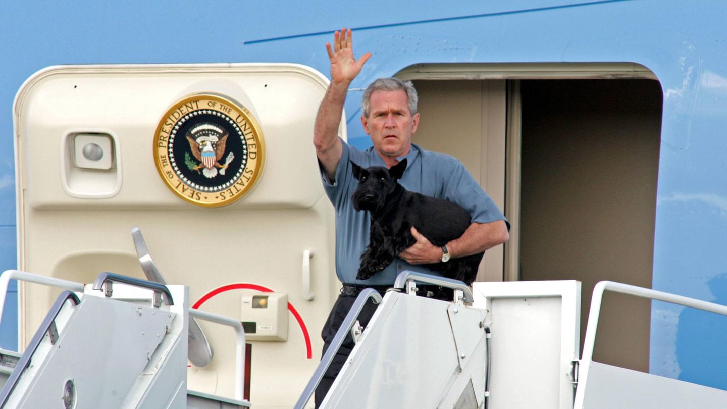 George W- Bush hält auf der Treppe eines Flugzeugs einen schwarzen Hund im Arm