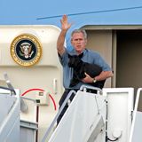 George W- Bush hält auf der Treppe eines Flugzeugs einen schwarzen Hund im Arm