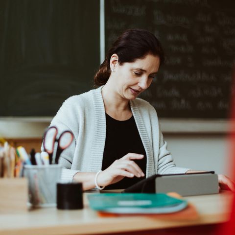 Eine Lehrerin sitzt am Pult und schaut in ihr iPad