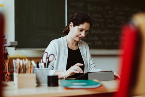 Eine Lehrerin sitzt am Pult und schaut in ihr iPad