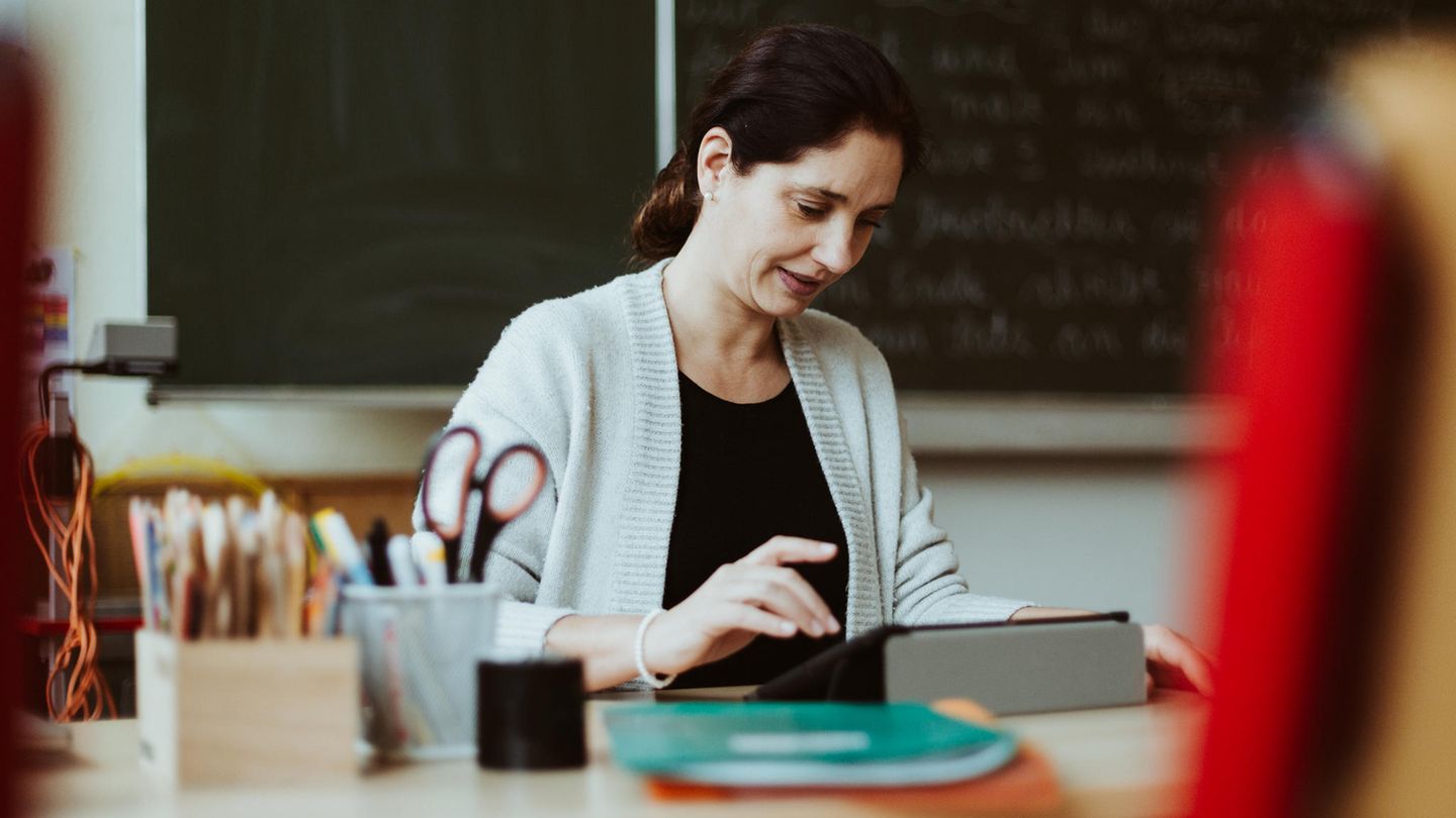 Eine Lehrerin sitzt am Pult und schaut in ihr iPad
