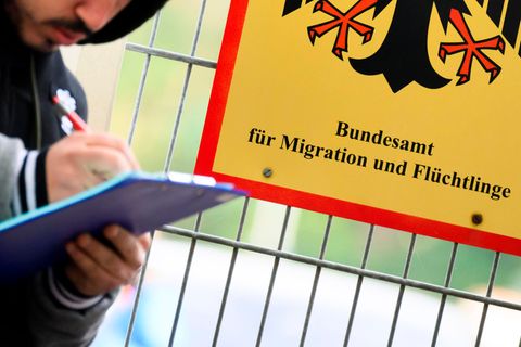 Ein Mann füllt ein Formular aus neben einem Schild vom Bundesamt für Migration und Flüchtlinge
