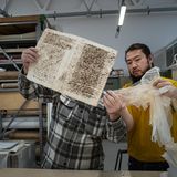 Ein Restaurator zeigt dem Eigentümer ein traditionelles Japanisches Papier, mit dem ein antikes Buch restauriert wurde.