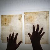 Eine Restauratorin hält mit den Händen zwei alte Papierdokumente auf einem Leuchttisch fest