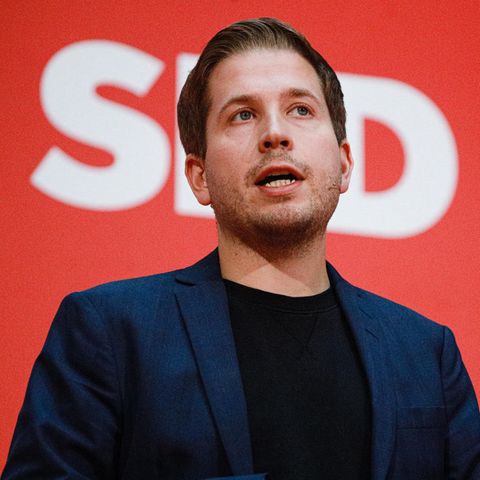 Kevin Kühnert spricht vor einer roten Wand mit weißem Logo der SPD