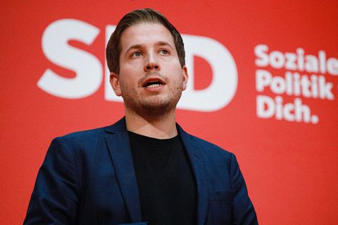 Kevin Kühnert spricht vor einer roten Wand mit weißem Logo der SPD