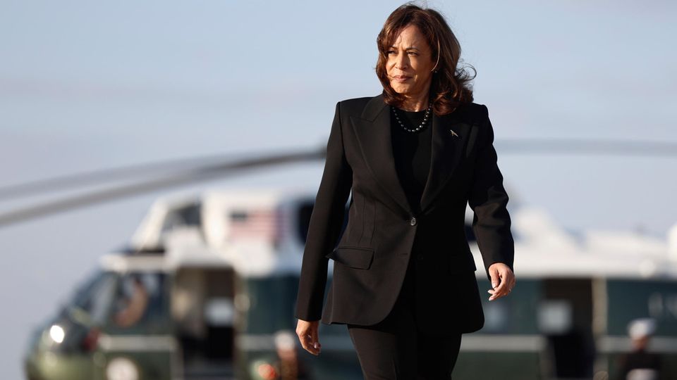 Kamala Harris geht auf den Betrachter zu auf dem Flugfeld. Im Hintergrund der Hubschrauber der Vizepräsidentin "Marine Two"