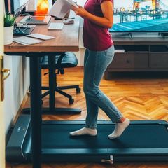 Junge Geschäftsfrau, die an einem ergonomischen Stehpult arbeitet, während sie auf einem Laufband geht