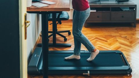 Junge Geschäftsfrau, die an einem ergonomischen Stehpult arbeitet, während sie auf einem Laufband geht