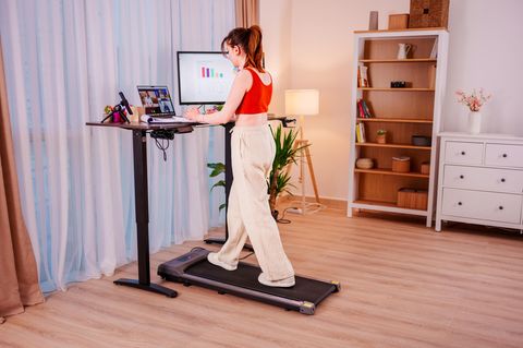 Junge Geschäftsfrau, die an einem ergonomischen Stehpult arbeitet, während sie auf einem Laufband geht