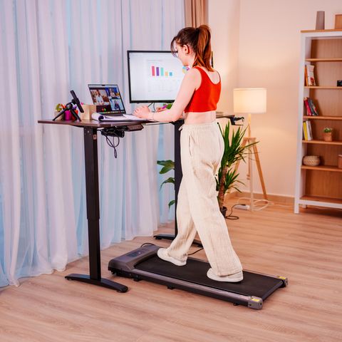 Junge Geschäftsfrau, die an einem ergonomischen Stehpult arbeitet, während sie auf einem Laufband geht