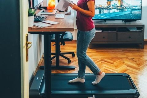Junge Geschäftsfrau, die an einem ergonomischen Stehpult arbeitet, während sie auf einem Laufband geht
