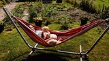 Eine Mutter liegt mit ihrem Kind im Schrebergarten in der Hängematte in der Sonne und stillt ihr Kind.