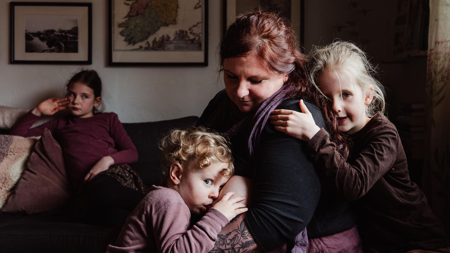 Eine Frau sitzt mit ihren drei Kindern im Wohnzimmer, eins davon wird gestillt