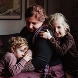 Eine Frau sitzt mit ihren drei Kindern im Wohnzimmer, eins davon wird gestillt