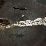 Ein Helikopter trägt Sandsäcke zu einem übergelaufenen Fluss