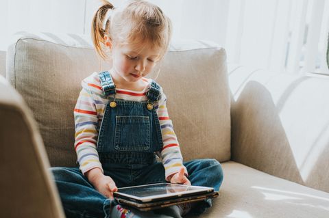Medienkonsum bei Kindern: kleines Mädchen sitzt mit Tablet auf dem Sofa